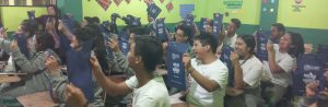 Estudiantes en una aula de clases con promocionales en las manos