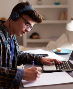 Un joven con audífonos utilizando una computadora y escribiendo.